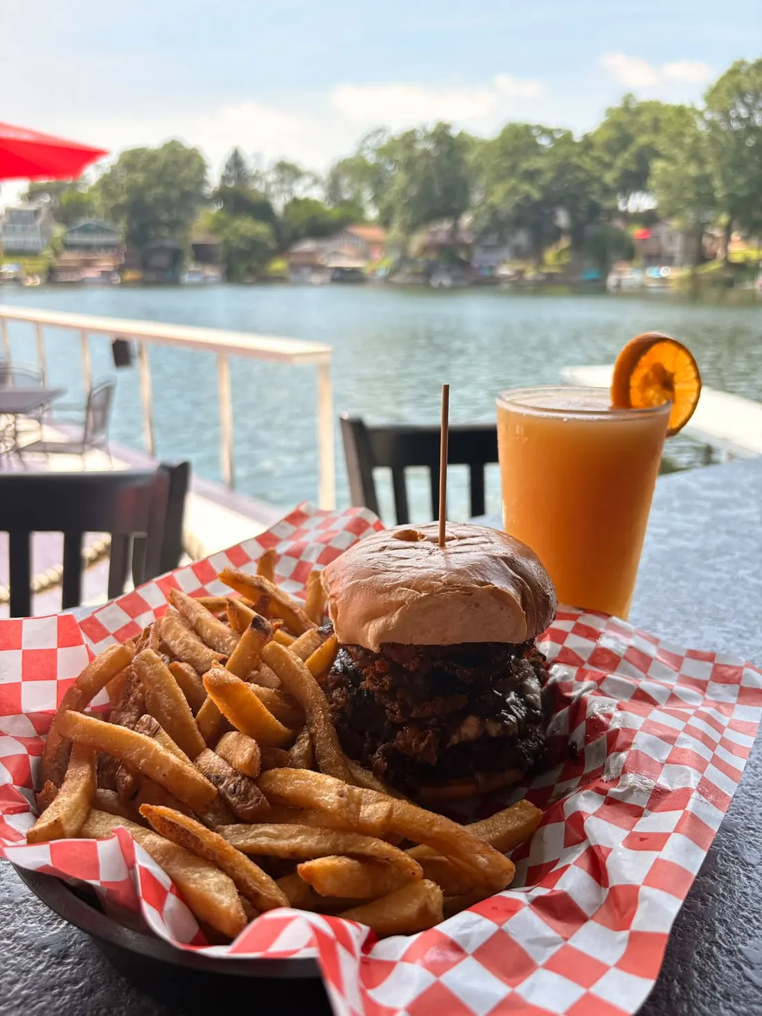 A burger and fries in a checkered-paper basket on the patio rail, with Portage Lakes behind it