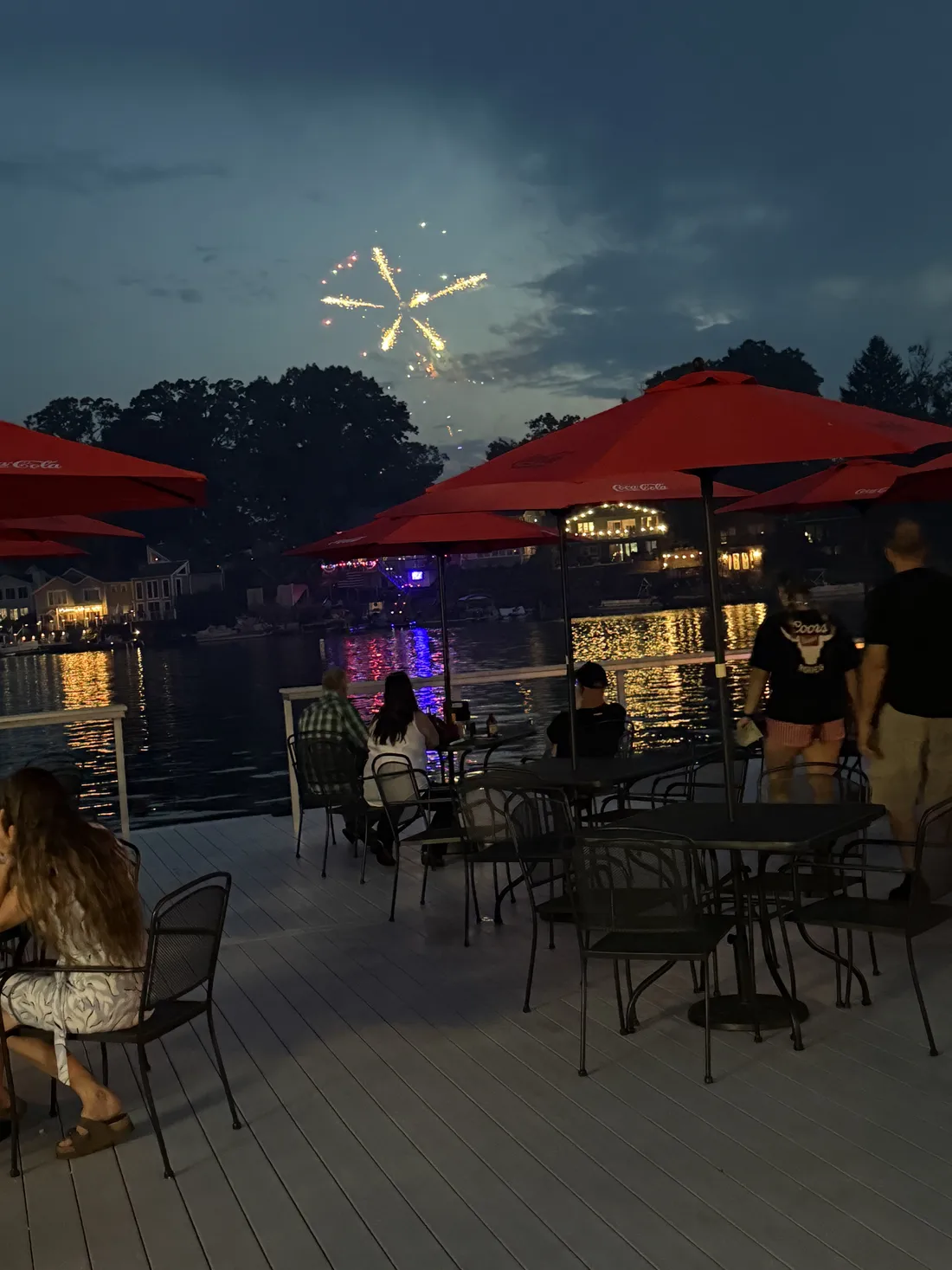Fireworks over Portage Lakes at dusk, watched from the patio under the red umbrellas