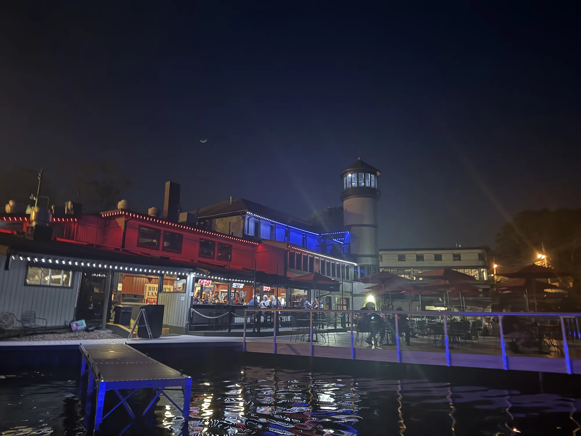 Harbor Lighthouse Grille at night from the water, the lighthouse tower lit up over the patio and docks